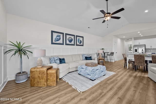 living room with ceiling fan, sink, light wood-type flooring, and vaulted ceiling