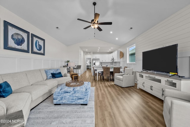 living room featuring ceiling fan, lofted ceiling, and light hardwood / wood-style flooring