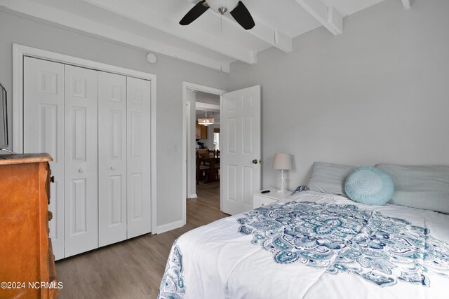 bedroom with a closet, black fridge, beam ceiling, wood-type flooring, and ceiling fan