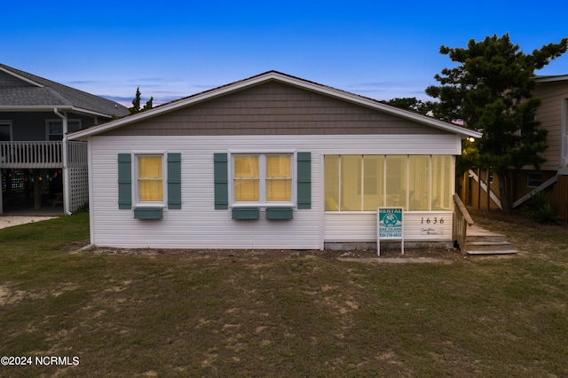 back house at dusk with a lawn and a sunroom