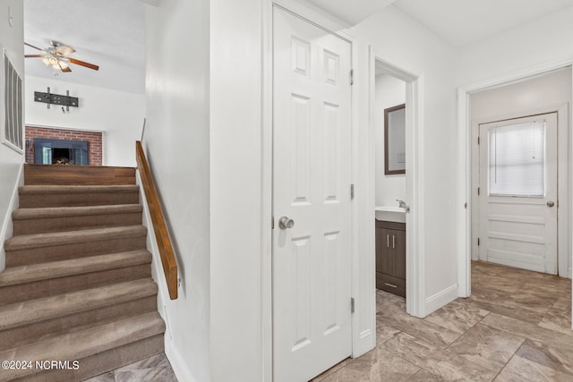 stairway featuring ceiling fan and a brick fireplace