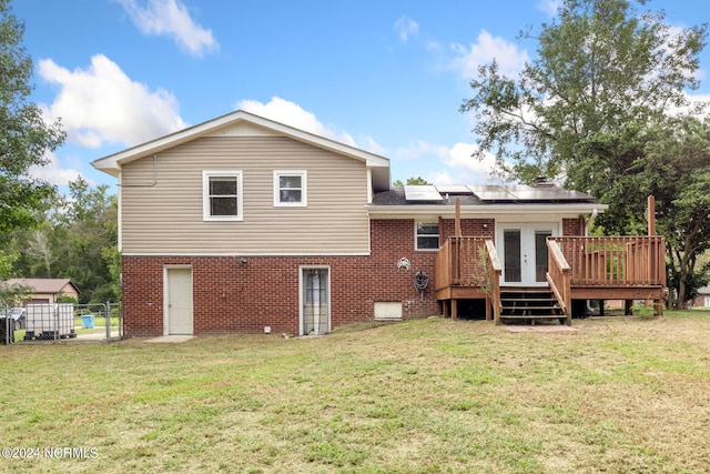 back of house with solar panels, a deck, and a lawn