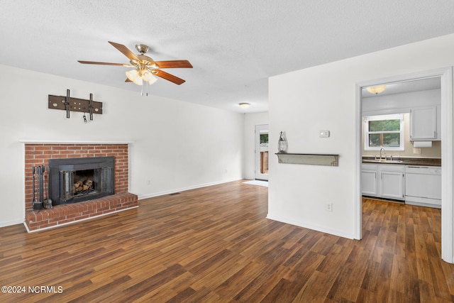 unfurnished living room with ceiling fan, sink, a brick fireplace, a textured ceiling, and dark hardwood / wood-style flooring