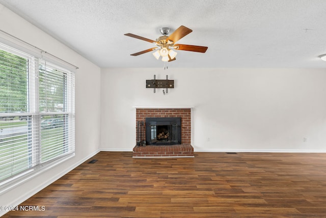 unfurnished living room with ceiling fan, a brick fireplace, a textured ceiling, and dark hardwood / wood-style floors