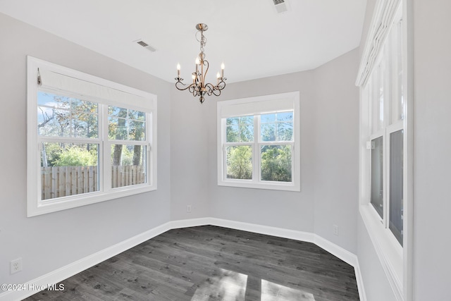 empty room with dark hardwood / wood-style floors, a wealth of natural light, and an inviting chandelier