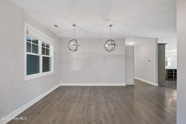 empty room with dark wood-type flooring and a notable chandelier