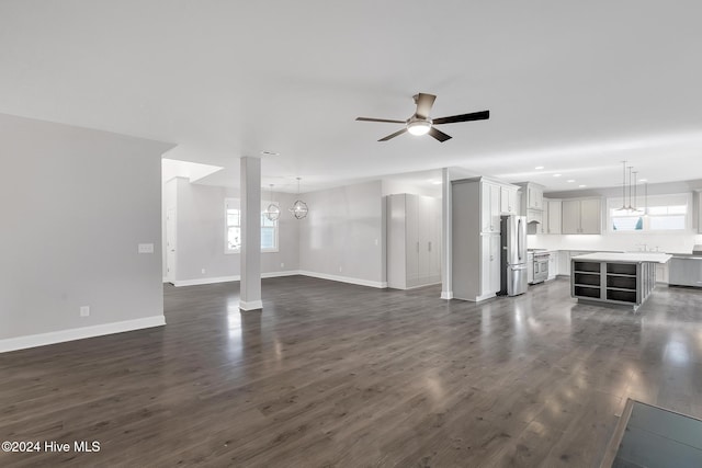 unfurnished living room with dark hardwood / wood-style floors, a healthy amount of sunlight, and ceiling fan with notable chandelier