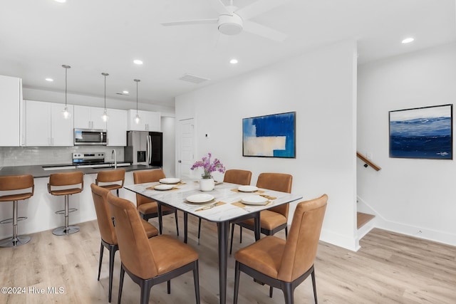 dining space featuring ceiling fan, sink, and light wood-type flooring