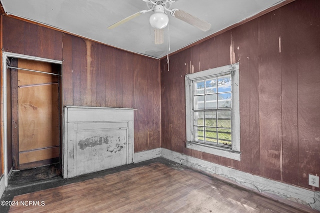 unfurnished bedroom with wooden walls, ceiling fan, and dark hardwood / wood-style floors