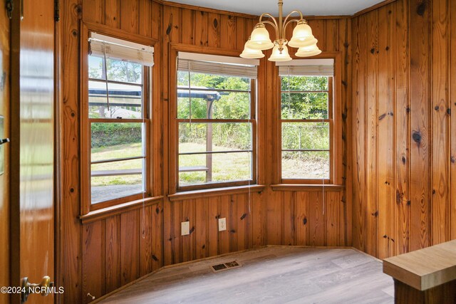 spare room featuring ornamental molding, wood walls, hardwood / wood-style floors, and a notable chandelier