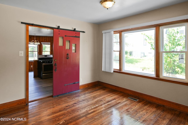 empty room with a barn door, a healthy amount of sunlight, and dark hardwood / wood-style flooring