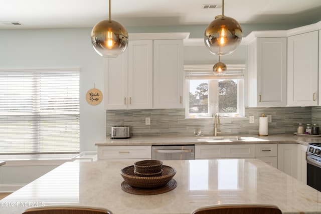 kitchen with tasteful backsplash, sink, white cabinetry, decorative light fixtures, and stainless steel dishwasher