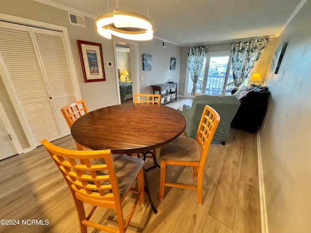 dining space with light hardwood / wood-style floors, ornamental molding, and a textured ceiling