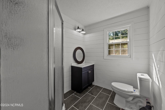 bathroom featuring vanity, a textured ceiling, a shower with shower door, toilet, and wood walls