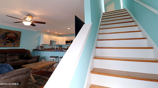 stairway with ceiling fan, sink, and crown molding