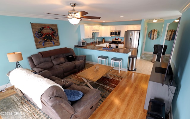 living room featuring ornamental molding, light wood-type flooring, ceiling fan, and sink