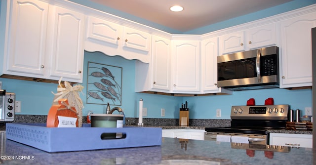 kitchen with white cabinets, stainless steel appliances, and dark stone counters