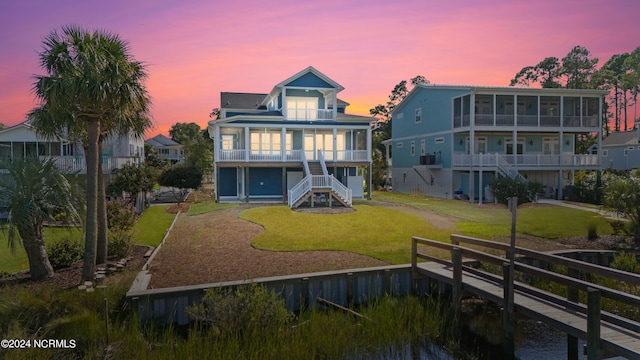 back house at dusk with a sunroom, a yard, and a balcony