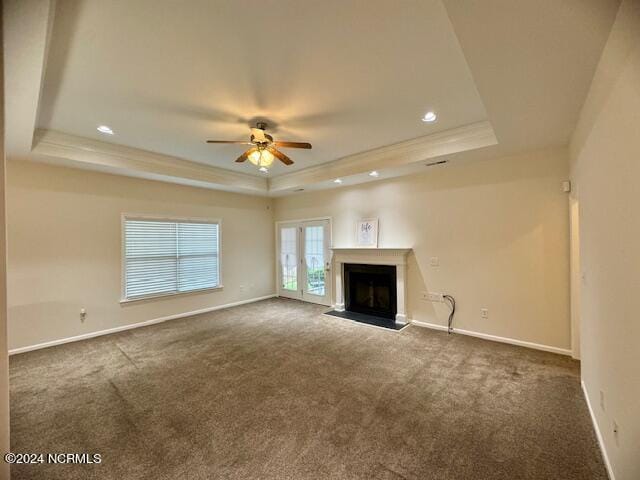 unfurnished living room featuring a tray ceiling, ceiling fan, french doors, and dark carpet