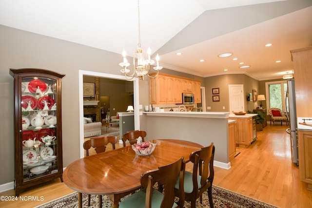 dining area featuring lofted ceiling, ornamental molding, a fireplace, and light wood-style floors