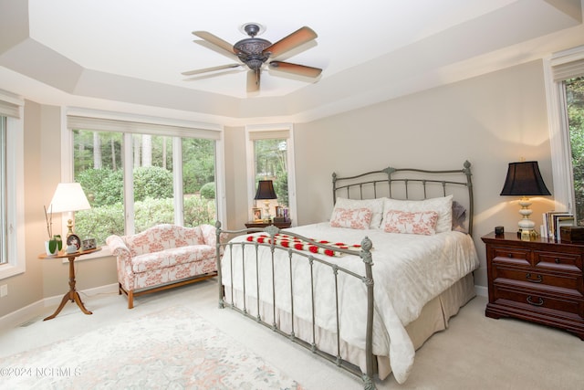 carpeted bedroom with baseboards, a tray ceiling, and a ceiling fan