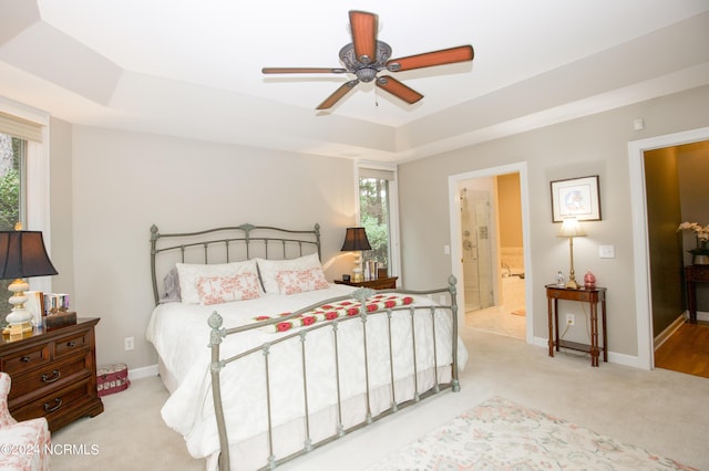 bedroom with baseboards, connected bathroom, light colored carpet, ceiling fan, and a tray ceiling