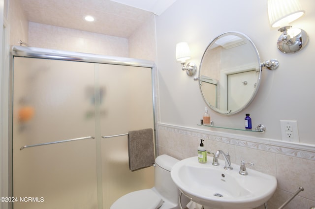 bathroom with a wainscoted wall, tile walls, toilet, a stall shower, and a sink