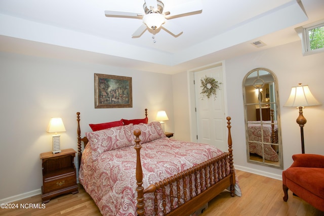 bedroom featuring a tray ceiling, visible vents, light wood-style flooring, and baseboards