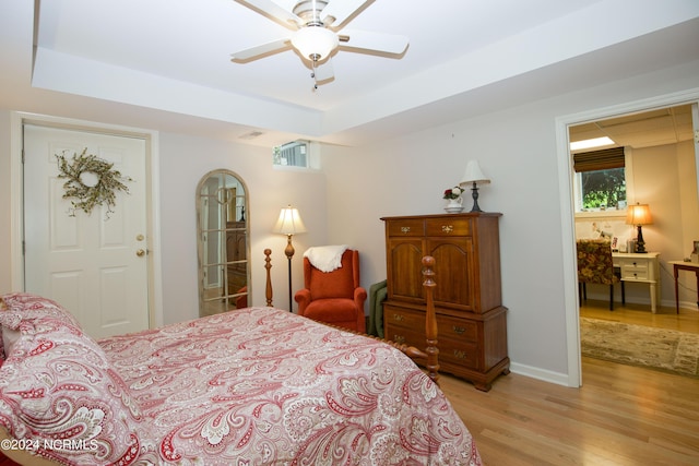 bedroom with a ceiling fan, a raised ceiling, light wood-style flooring, and baseboards