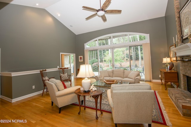 living area featuring baseboards, a ceiling fan, light wood-style flooring, a fireplace, and high vaulted ceiling