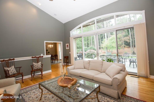 living area with high vaulted ceiling, light wood-style flooring, visible vents, and an inviting chandelier