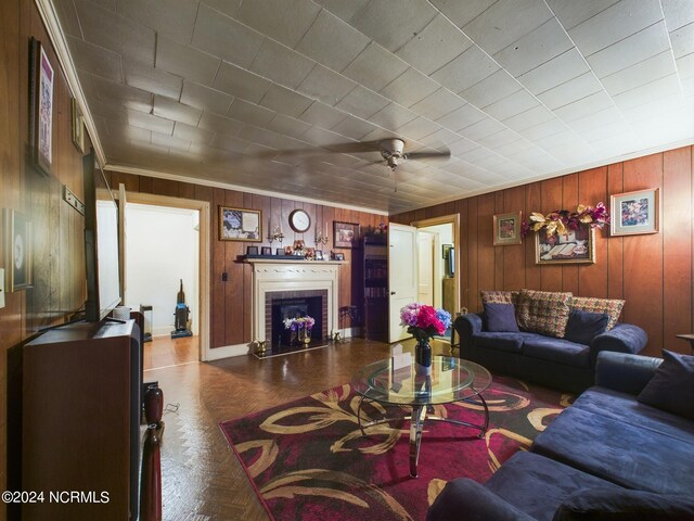 living room with a fireplace, wooden walls, ceiling fan, and dark parquet floors