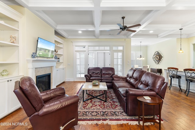 living room with ceiling fan, coffered ceiling, built in features, a high end fireplace, and beamed ceiling