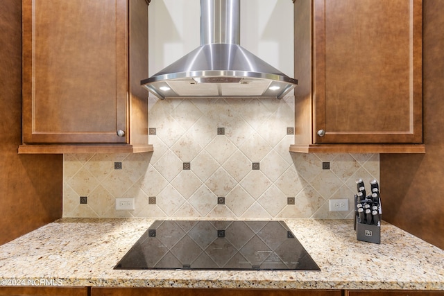 kitchen featuring wall chimney exhaust hood, light stone counters, decorative backsplash, and black electric cooktop