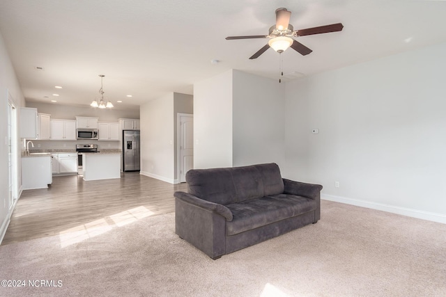 living room featuring ceiling fan with notable chandelier, light hardwood / wood-style floors, and sink