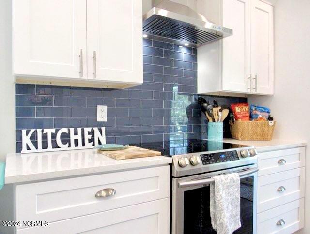 kitchen featuring backsplash, wall chimney exhaust hood, white cabinetry, and stainless steel range with electric cooktop