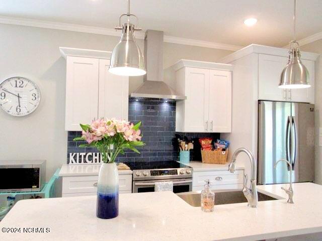 kitchen with appliances with stainless steel finishes, hanging light fixtures, and wall chimney range hood