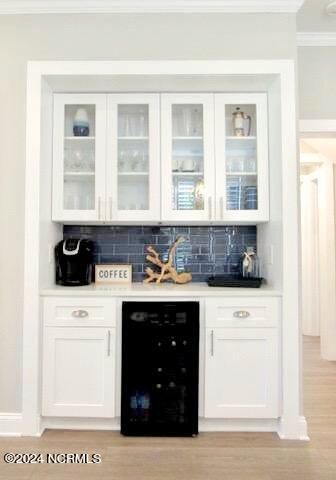 bar with decorative backsplash, light hardwood / wood-style floors, wine cooler, and white cabinets