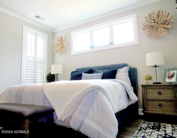 bedroom featuring wood-type flooring, multiple windows, and crown molding