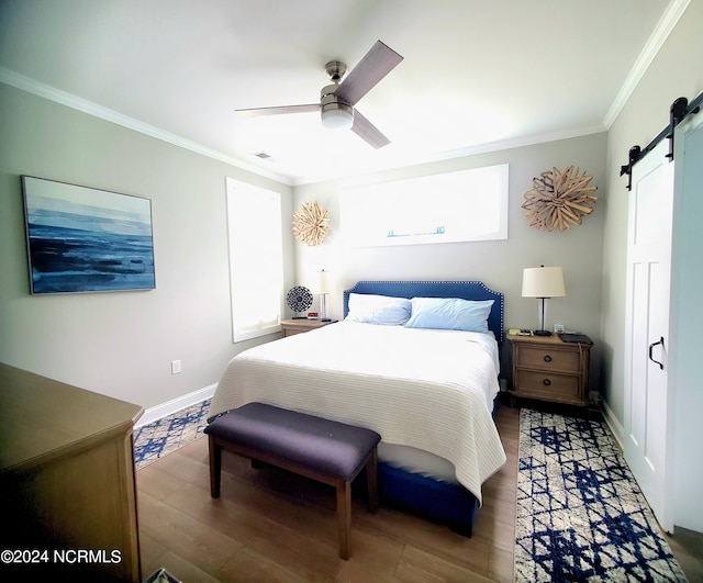 bedroom featuring a barn door, wood-type flooring, crown molding, and ceiling fan