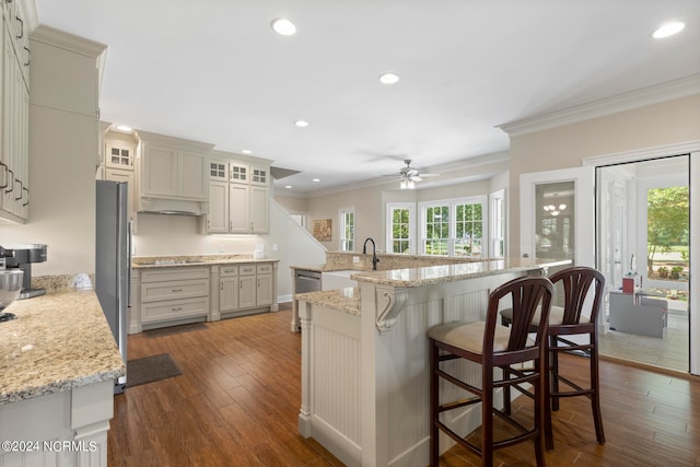 kitchen with dark wood-type flooring, sink, crown molding, a kitchen breakfast bar, and a kitchen island