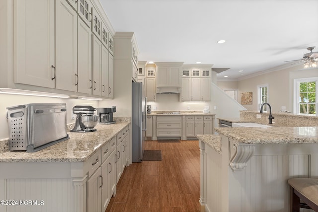 kitchen featuring sink, crown molding, stainless steel fridge, light stone counters, and a kitchen bar