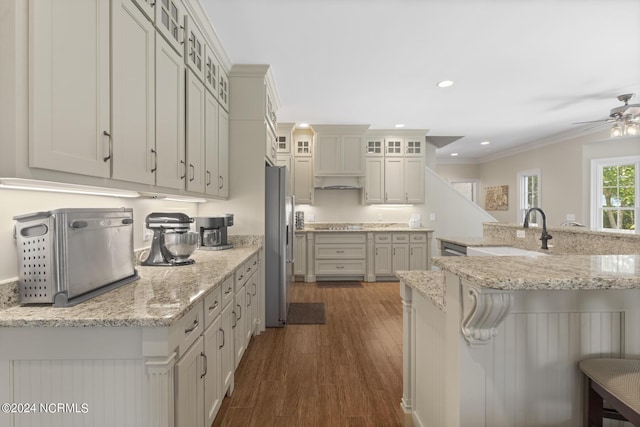 kitchen featuring stainless steel fridge, a ceiling fan, a kitchen bar, dark wood finished floors, and a sink