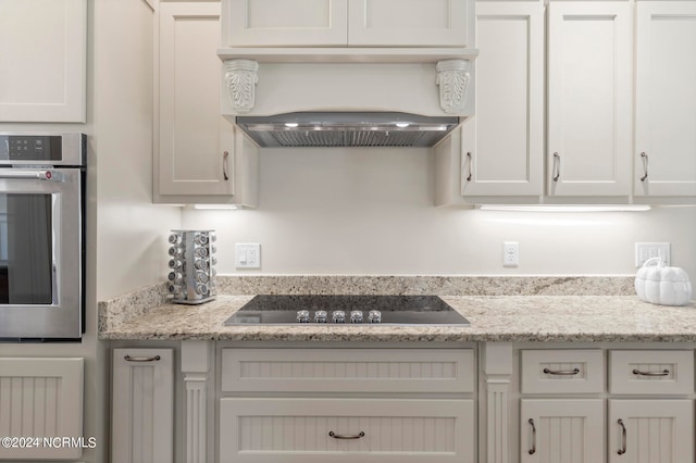 kitchen with white cabinets, custom range hood, black electric stovetop, and oven