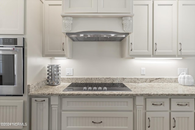 kitchen featuring light stone counters, custom range hood, black electric cooktop, and stainless steel oven
