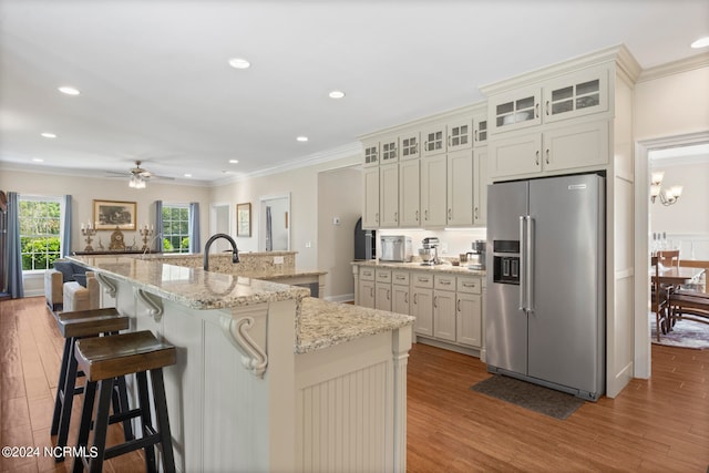 kitchen featuring an island with sink, a breakfast bar area, high end refrigerator, hardwood / wood-style flooring, and light stone countertops