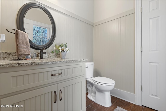 half bath with vanity, baseboards, toilet, and wood finished floors