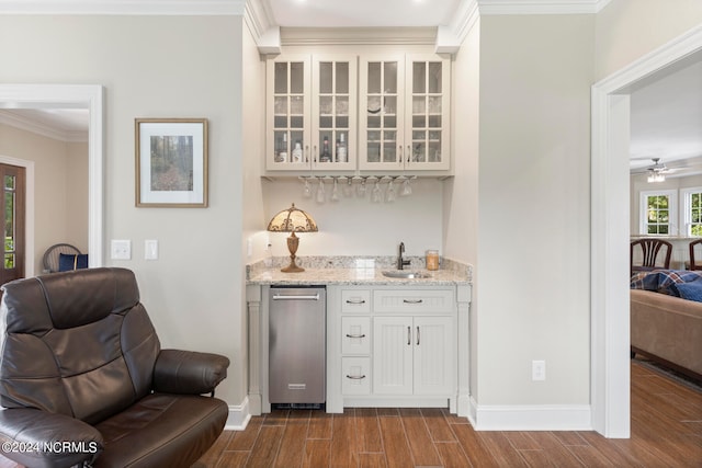 bar with sink, ceiling fan, white cabinetry, light stone counters, and ornamental molding