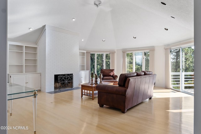 living room with lofted ceiling, built in features, a textured ceiling, a fireplace, and light hardwood / wood-style floors