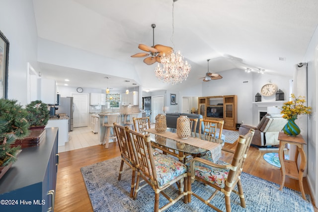 dining area with ceiling fan with notable chandelier, light hardwood / wood-style flooring, and vaulted ceiling